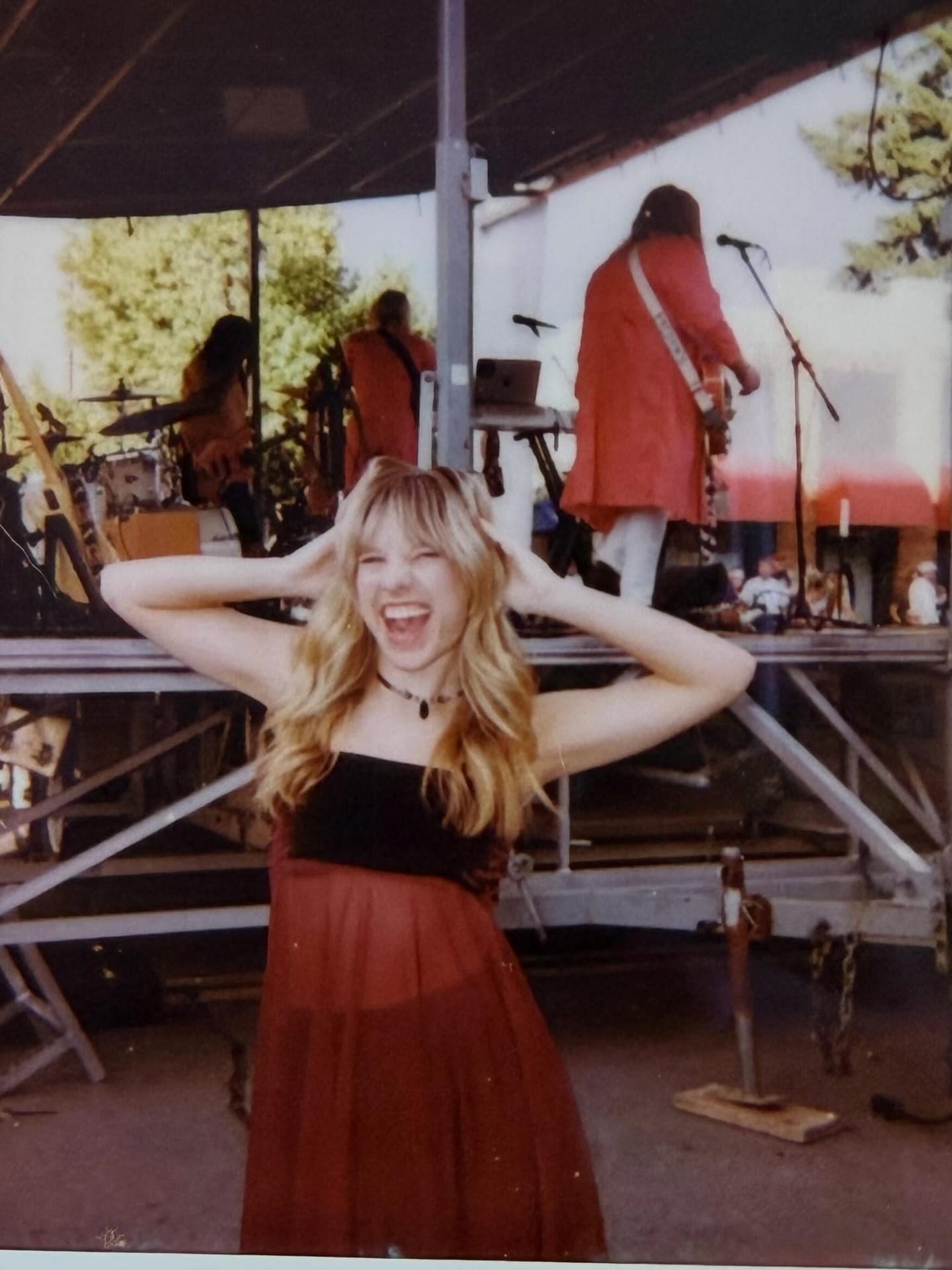 Tiffany Johnson laughing in front of an outdoor stage in a red dress while her band plays behind her