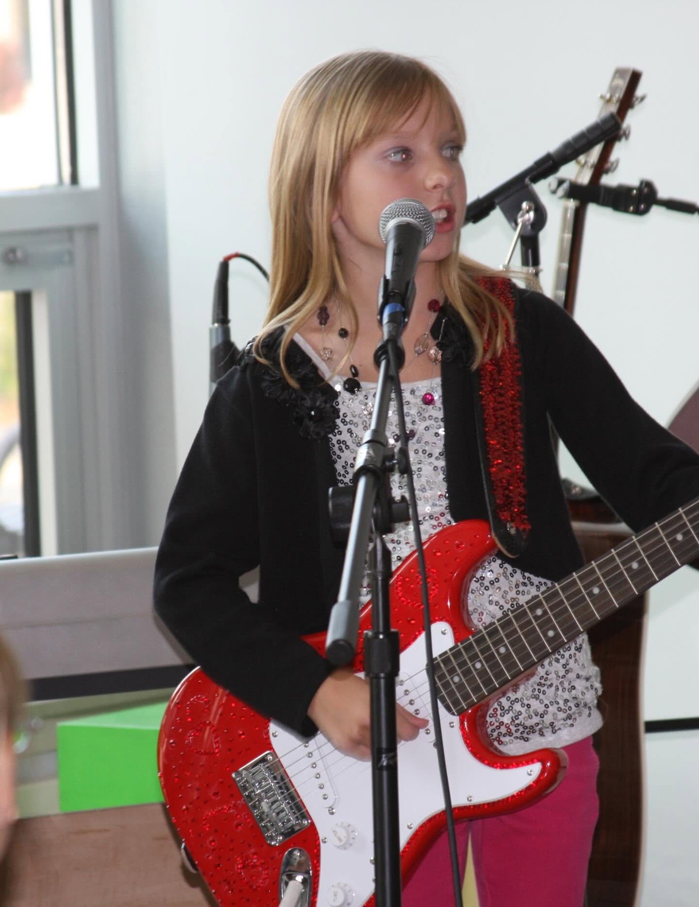 A young Tiffany Johnson singing at a microphone with a red sparkly electric guitar